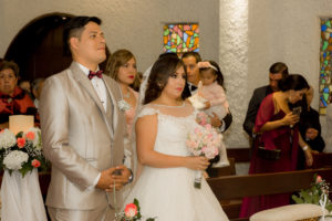 Novio mirando al padre muy feliz y novia con vestido blanco y el ramo sosteniéndolo en las manos.