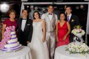 Pareja de esposos en foto familiar, acompañados por sus padres y testigos matrimoniales, con la torta de la fiesta y decoración