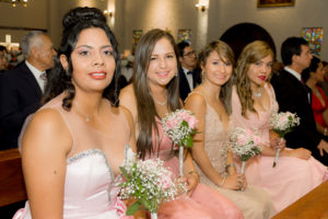 4 damas de honor sonrientes sentadas en la iglesia posando para la foto vestidas con un vestido de noche color palo de rosa y sus ramos