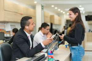 Pareja de trabajadores con celular en la mano, conversando en oficina mientras trabajan.