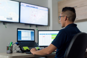 Ingeniero de sistemas trabajando en computador de dos pantallas, con análisis de fondo de información en televisores