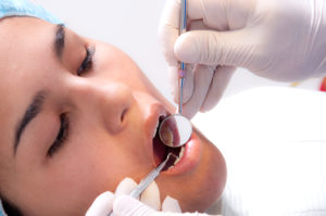 Mujer en control de odontología con pinza y espejo en la boca