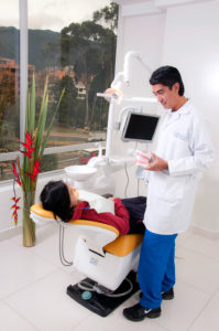 Odontólogo atendiendo a cliente, con vista a la ciudad, explicándole un correcto lavado de dientes.