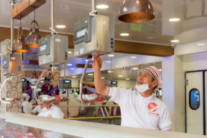 Hombre con camisa blanca y tapabocas trabajando en carnicería elite, pesando el producto en una pesa digital