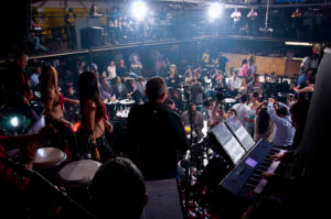 Grupo de salsa presentándose en discoteca mientras los asistentes los miran y bailan felices