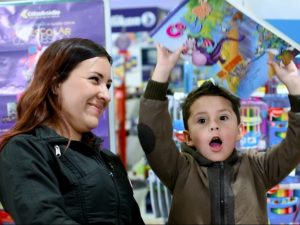 Niño feliz recibiendo kit escolar mientras mamá sonríe.