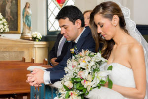 Pareja de esposos en el día de su boda arrodillados en la iglesia con los ojos cerrados.