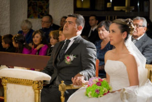 Pareja de novios en la igledia, esperando la bendición del padre.