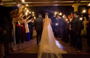 Pareja de esposos saliendo de la iglesia en la noche, mientras sus invitados les hacen un camino con chispitas mariposas.