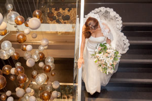 Mujer vestida de novia bajando las escaleras al lado de imponente lampara