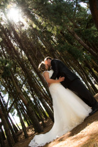 Pareja de novios besandose en un bosque de pinos altos.