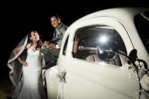 PAreja de novios encima de carro antiguo posando en el día de su boda.