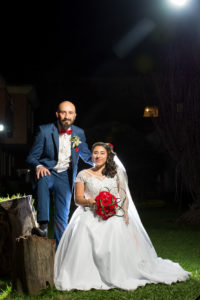 Mujer sentada con vestido de novia y pareja vestido de esmoquin al lado de ella en la noche.